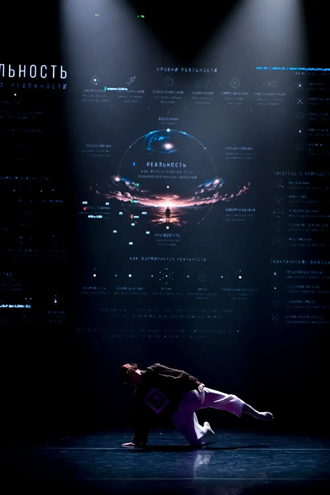 A dancer close to the floor beneath light beams and a digital projection.