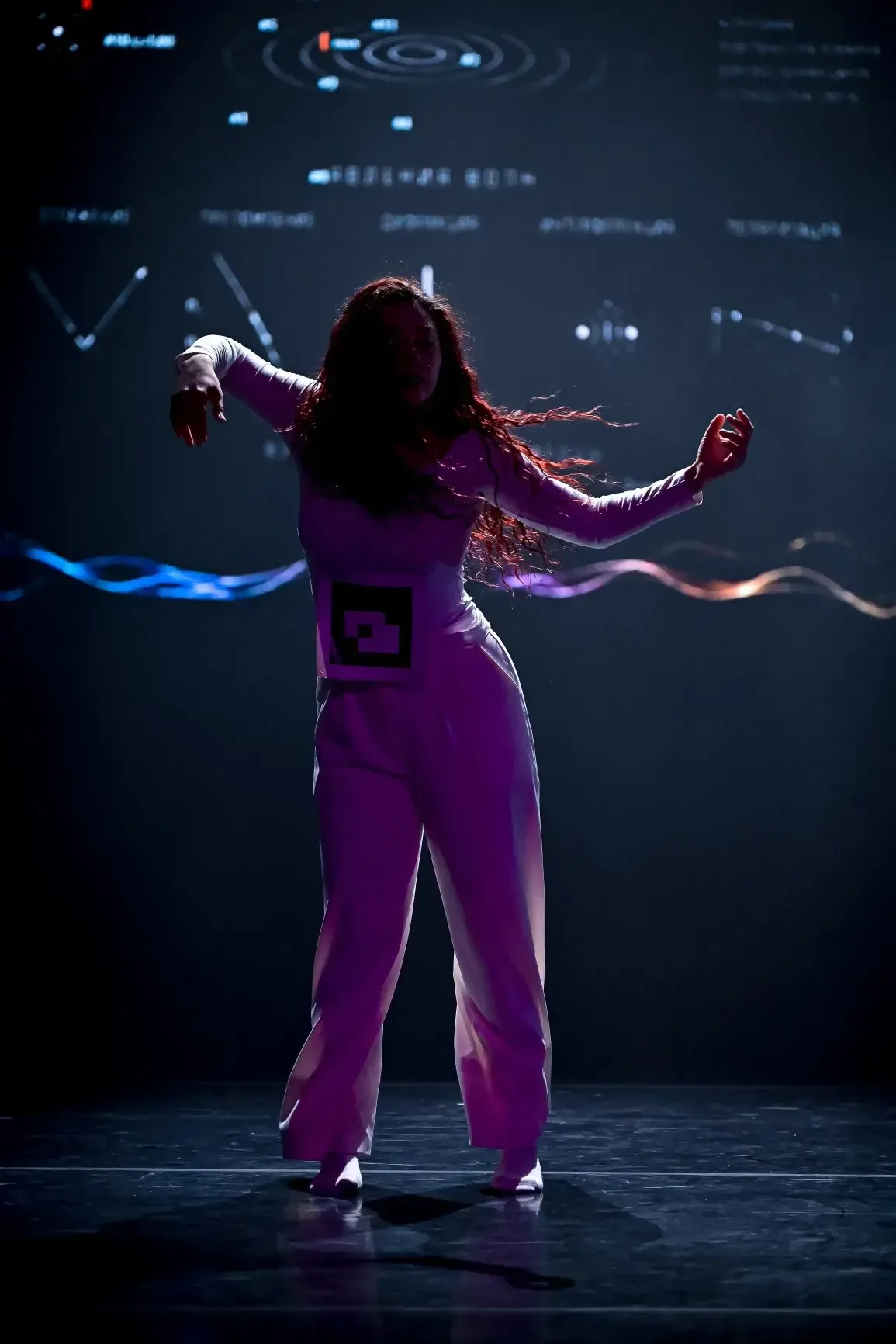 A dancer with outstretched arms in front of a projection.