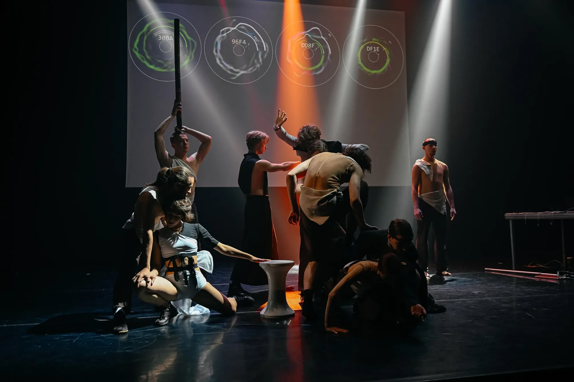 Participants and dancers under coloured beams in front of circular projections.
